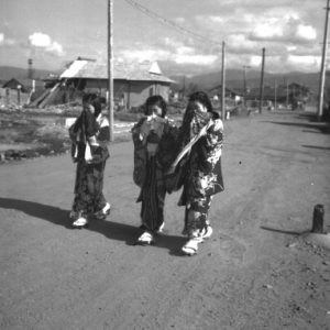 Three girls in traditional Japanese kimotos walking along a dirty road.
