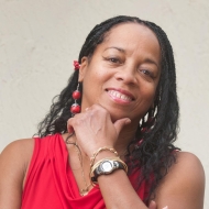 Headshot of a Black woman in a red top, smiling with her hand on her chin.